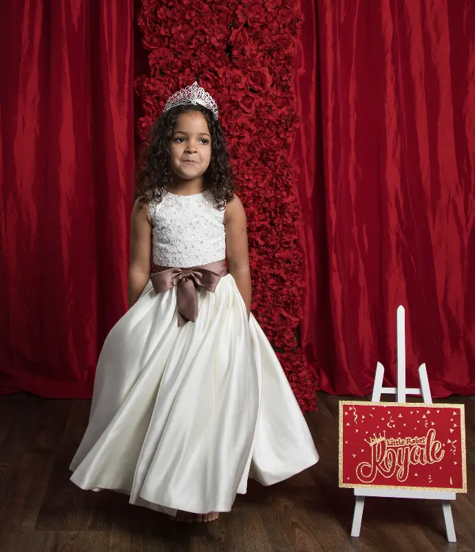 Sleeveless satin A-line ball gown with a pearl flowered lace top, fronted bow belt and decorated colour tail panel